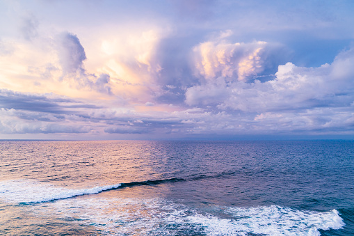 Bali, aerial shot of the turquoise ocean surface, waves and cloudy sky.