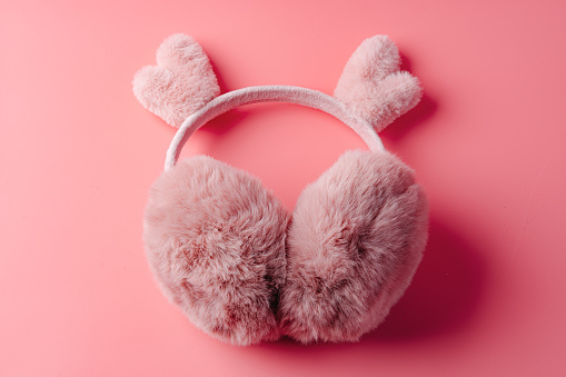 Fluffy warm pink earmuffs on pink background top view