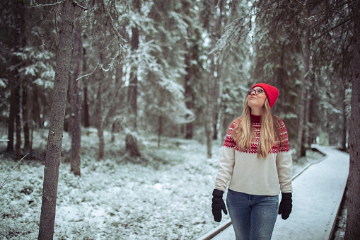 A cheerful female tourist walks along a path and looks at nature during a snowy winter day