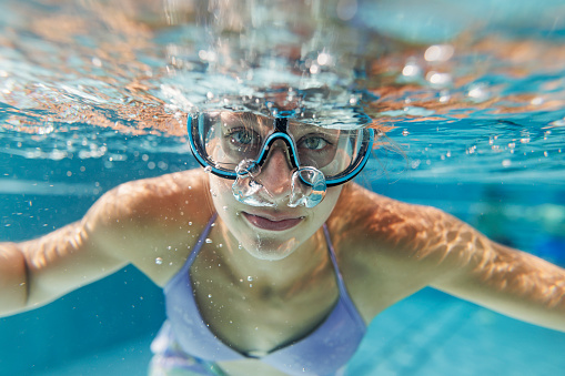 Underwater portrait of a teenage girl enjoying swimming pool. The girl is looking at the camera.
Canon R5