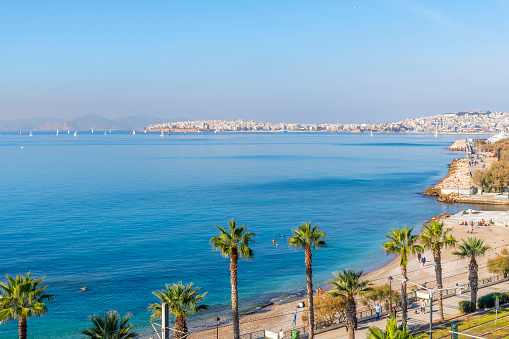 View from a balcony of the coastline and waterfront promenade along the Athenian Riviera at Palaio Faliro, with the city of Piraeus, Greece in view in the distance.