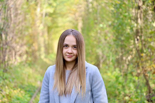 Portrait of a model girl in a gray coat. A beautiful girl with long hair and a gray coat in the forest among the trees.