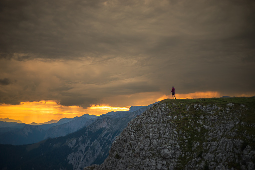 Male hiker looking at beautiful landscape scenery while standing on top of mountain against cloudy sky