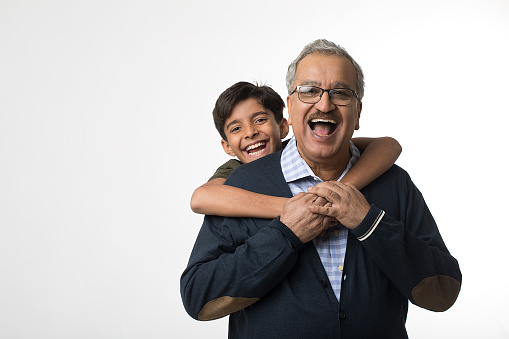 Portrait of laughing grandson embracing old grandfather from behind