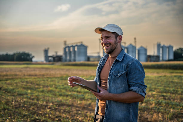 contadino maschio felice che usa la tavoletta digitale nel campo contro il cielo - farmer foto e immagini stock