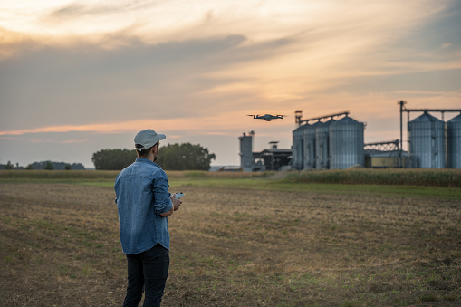 Male farmer operating flying drone with remote controller over agricultural field