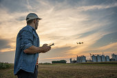 Male farmer with remote controller flying drone above farmland