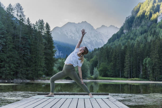 istock Woman practicing reverse warrior pose on pier by lake in forest 1451087402