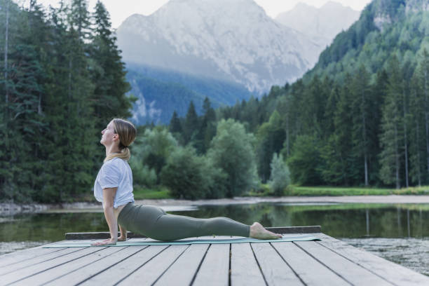 istock Female yogi practicing cobra pose on pier by lake in forest 1451087654