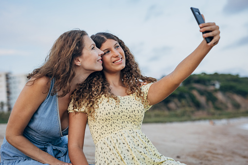 Two people, mother with her teenage daughter taking a selfie on the beach by the sea.