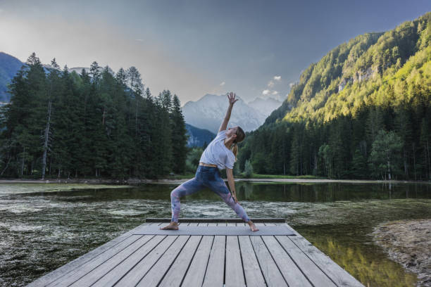 istock Woman practicing reverse warrior pose on pier amidst lake 1451088419