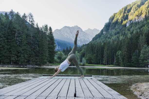 istock Woman with leg up practicing downward facing dog pose on pier by the lake 1451088421