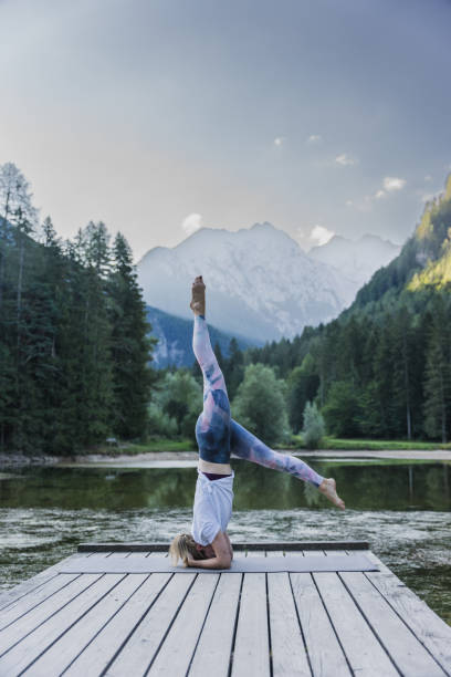 istock Woman doing headstand and splits on pier by lake at forest 1451088544