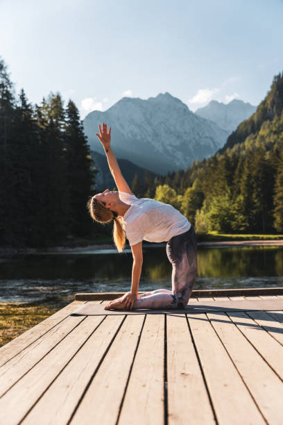 istock Woman with hand raised practicing camel pose on pier by lake during vacation 1451088554