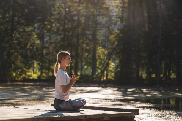 istock Woman meditating in prayer position while sitting on pier by lake 1451088667