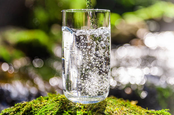 istock Clean water filling in drinking glass over moss covered rock 1451088840
