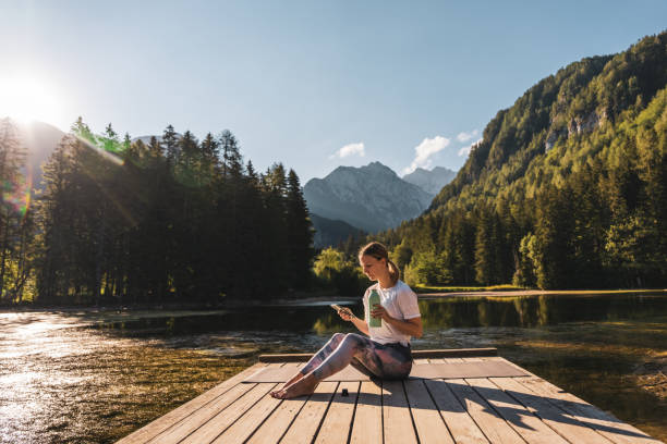 istock Tired woman with bottle using smart phone while sitting on pier 1451089074