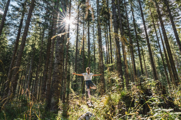 istock Woman with arms outstretched meditating in tree pose at forest 1451089770