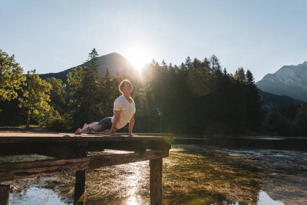 istock Woman practicing cobra pose on pier by lake in forest during sunny day 1451090219