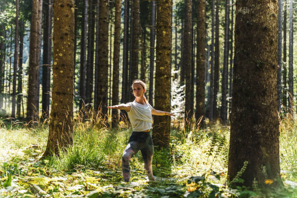 istock Woman practicing warrior 2 pose amidst plants and trees in forest 1451090541
