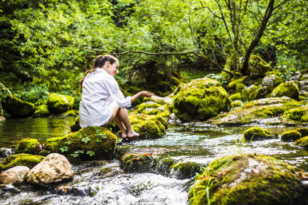 istock Woman playing with river water while sitting on rock 1451090590