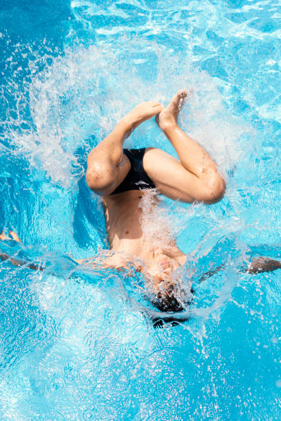 istock boy jumping into the pool making a big splash. Boy enjoying the pool in summer, throwing himself on his back splashing the pool water. Somersault in the pool to make a splash 1451090872