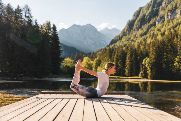 istock Woman practicing bow pose on pier amidst lake in forest during getaway 1451090940