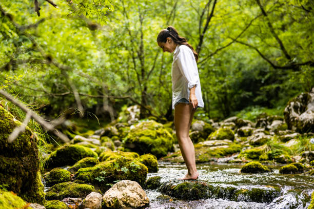 istock Woman standing on rock amidst flowing river in rainforest 1451090942