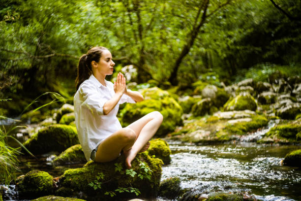 Young woman with eyes closed meditating while sitting on mossy rock against trees in rainforest during vacation