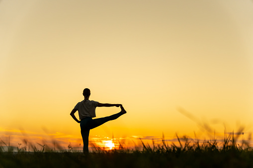 Rear view of silhouette young woman practicing hand to big toe pose on landscape with sky in the background at sunrise