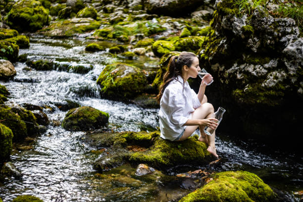 istock Woman drinking water while sitting on rock amidst river 1451091697