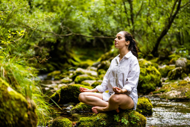 женщина медитирует в позе лотоса на мшистой скале в лесу - zen like nature breathing exercise sitting стоковые фото и изображения