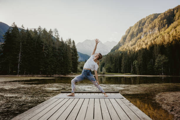 istock Woman practicing reverse warrior pose on pier by lake in forest 1451092259