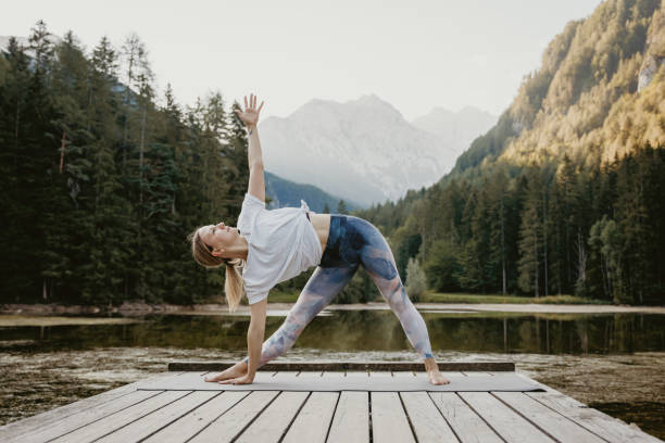 istock Dedicated woman practicing triangle pose on pier by lake in forest 1451092367