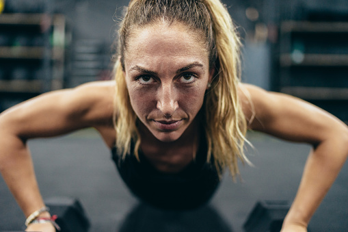 Close up photo of a strong woman doing push-ups using dumbbells in a gym