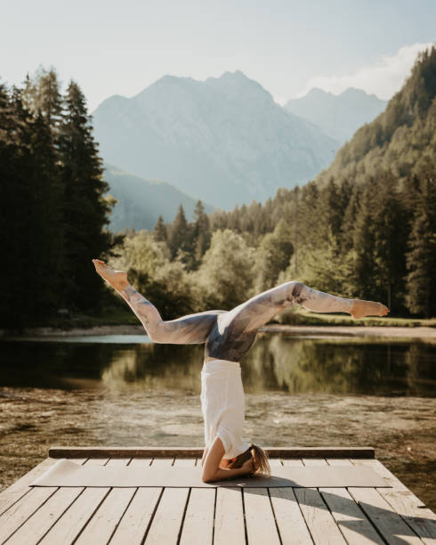 istock Female yogi doing headstand and splits on pier over lake at forest 1451093341