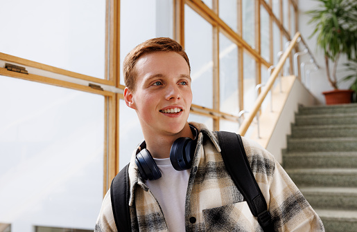 Smiling guy with headphones standing in college and looking away