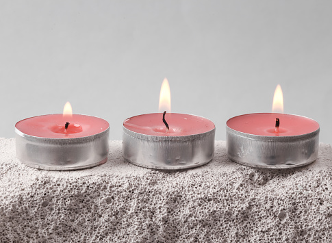 Flaming scented tea candles on stone. Gray background. Minimal concept.