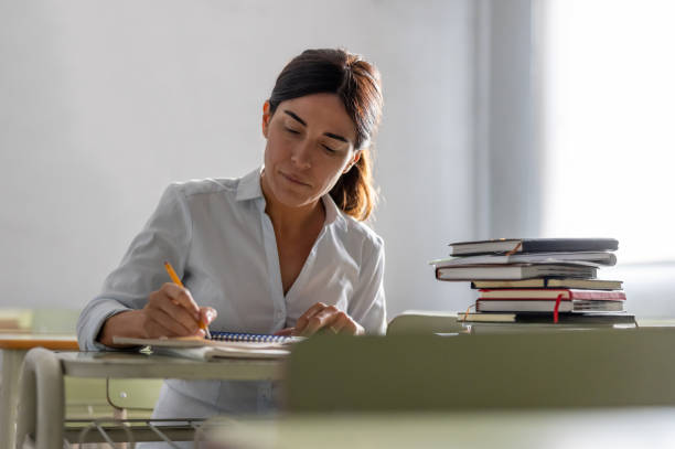 donna adulta che torna a scuola e scrive nel suo quaderno - grading foto e immagini stock