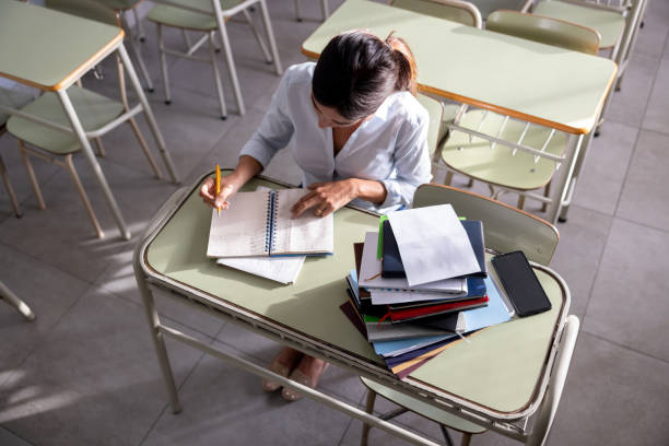 professor que trabalha na escola classificando alguns exames enquanto está sentado em uma mesa - grading teacher desk writing - fotografias e filmes do acervo