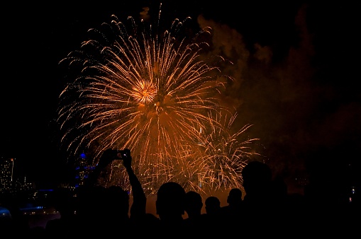 Tourists celebrate at the daily Niagara Falls firework display. Smartphones at the ready to capture the vibrant fireworks display each evening at the Niagara Falls overlook. Shadows of partiers against the orange pyro technique.