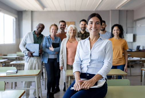 Happy Latin American female teacher in the classroom with a group of students and looking at the camera smiling - education concepts