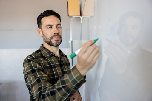 Latin American teacher writing with a market on a whiteboard - education concepts