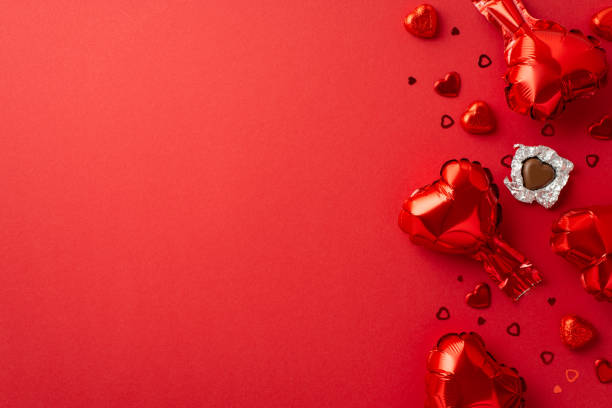 saint valentine's day concept. top view photo of heart shaped balloons unwrapped chocolate candies and confetti on isolated red background with empty space - valentines day candy chocolate candy heart shape imagens e fotografias de stock