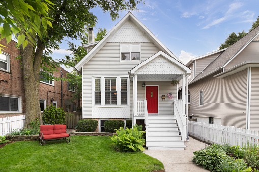 Chicago, IL, USA - June 3, 2019: A beautiful white house with a small front porch and red front door surrounded be a nicely landscaped yard and white picket fence.