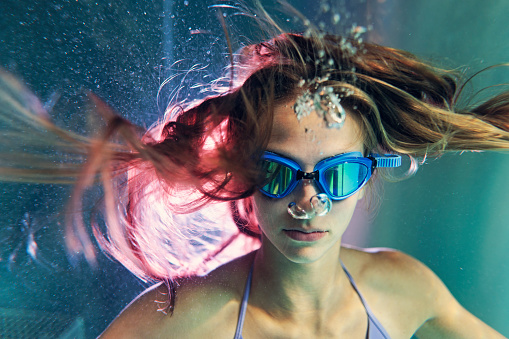 Underwater portrait of a teenage girl enjoying indoors swimming pool. The girl is looking at the camera.\nCanon R5