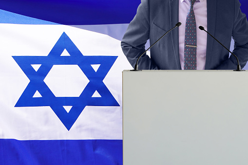 Tribune with microphone and man in suit on Israel flag background. Businessman and tribune on Israel flag background. Politician at the podium with microphones background Israel flag. Conference