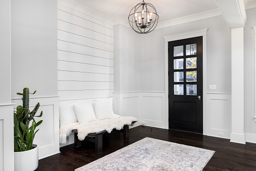 A beautiful foyer entrance with a light hanging above the dark hardwood floors, a bench in front of a shiplap wall, and a dark door with windows.