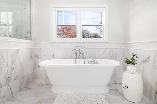 A luxurious bathroom with a standalone bathtub and chrome faucet surrounded by marble tiles on the floor and walls.