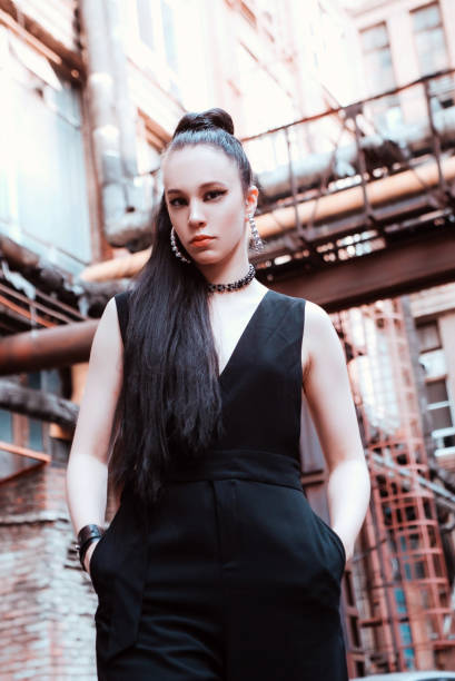 Portrait of lovely girl near a rusty fence. Stylish young woman dressed in the black hat, blouse, skirt, leggings and sunglasses